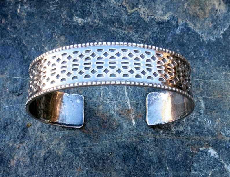 May include: A silver bracelet with a geometric pattern and a beaded edge.