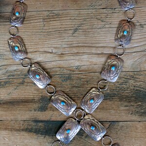 May include: A silver chain belt with rectangular turquoise stones set in each link. The belt is laid out on a wooden surface.