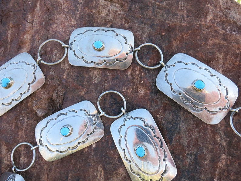 May include: A silver belt with turquoise stones and decorative designs. The belt is made up of rectangular links connected by silver rings.