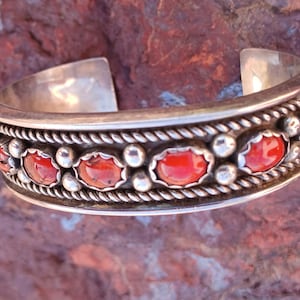 May include: A silver bracelet with a row of red coral stones set in a silver rope design.