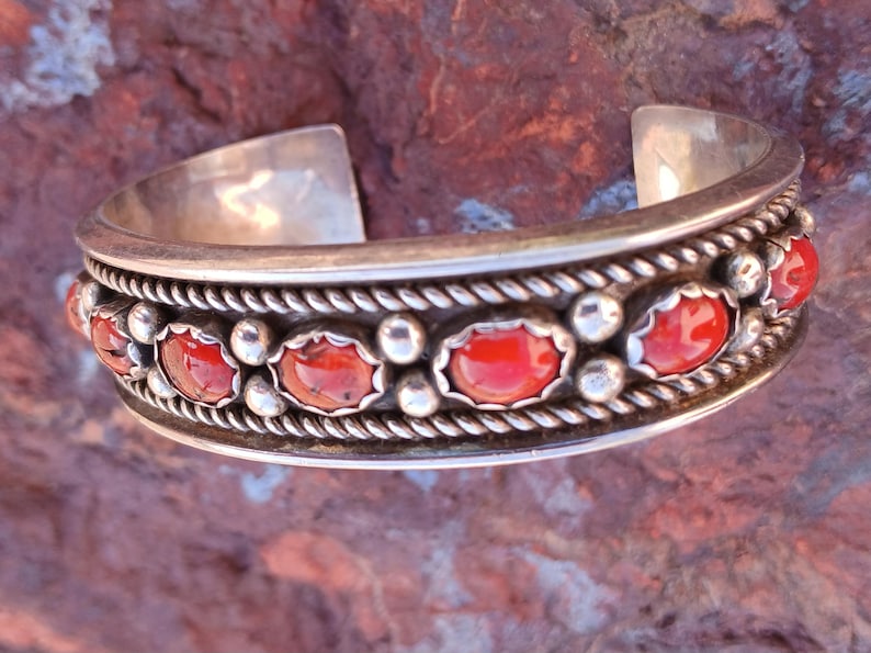 May include: A silver bracelet with a row of red coral stones set in a silver rope design.