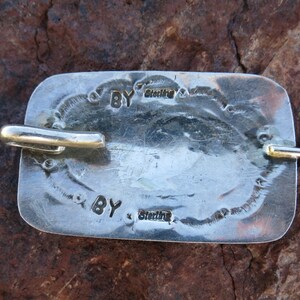 May include: Close-up of a silver belt buckle with the inscription "BY Sterling" on the back.