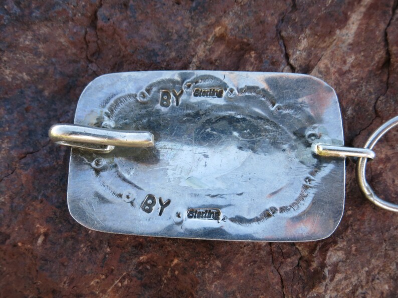 May include: Close-up of a silver belt buckle with the inscription "BY Sterling" on the back.