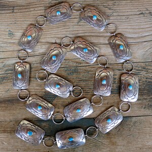 May include: A silver belt with turquoise stones set in rectangular silver plaques. The belt is made up of 15 plaques connected by silver rings.