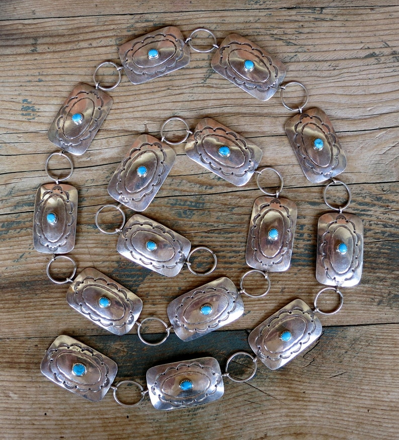 May include: A silver belt with turquoise stones set in rectangular silver plaques. The belt is made up of 15 plaques connected by silver rings.