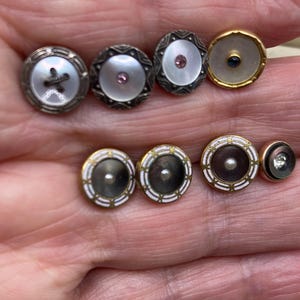 May include: A selection of antique buttons with diverse designs. The buttons incorporate mother-of-pearl, gemstones, and decorative metal detailing. Some have elaborate patterns and settings, displaying a variety of styles and colours, including silver, gold, and white.