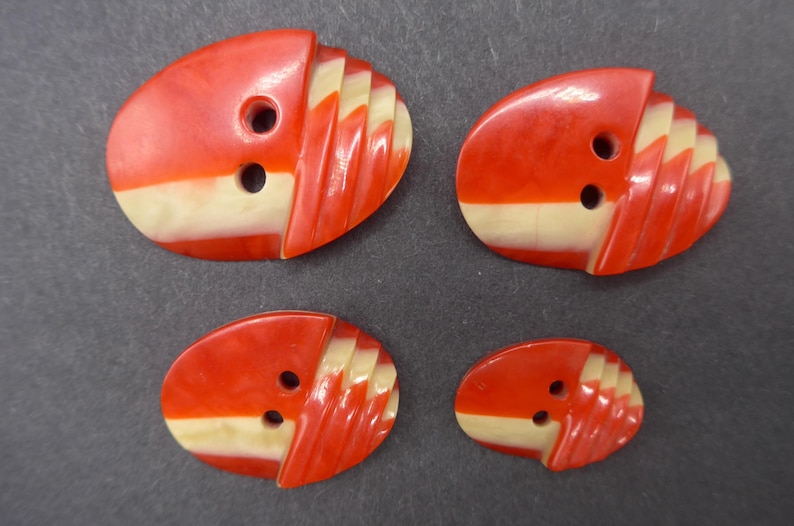 Puede incluir: Cuatro botones vintage de varios tama&ntilde;os. Cada bot&oacute;n tiene forma ovalada con una parte superior roja y una inferior color crema. La secci&oacute;n roja tiene un dise&ntilde;o acanalado. Cada bot&oacute;n tiene dos agujeros para coser.