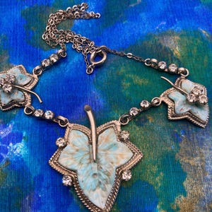May include: Vintage silver-tone necklace featuring leaf-shaped pendants with a light blue and white marbled design. The necklace has a delicate chain with clear rhinestone accents and a central leaf pendant.