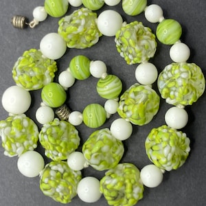 May include: A necklace featuring a repeating pattern of solid white glass beads and textured lime green and white speckled glass beads. The beads are strung on a cord and secured with a metallic screw-type barrel clasp at the end of the strand.