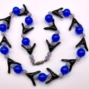 May include: A vintage necklace featuring blue glass beads, black arrow-shaped accents, and small, pale pink beads. The necklace has a silver-tone magnetic clasp. The design is symmetrical and eye-catching.