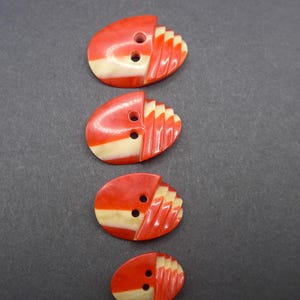 Puede incluir: Cuatro botones ovalados vintage. Cada bot&oacute;n es rojo con una franja crema y un dise&ntilde;o en forma de abanico en un lado. Los botones tienen dos agujeros para coser.
