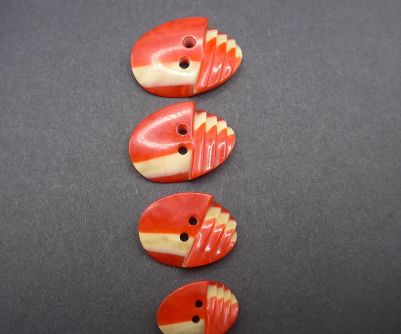 Puede incluir: Cuatro botones ovalados vintage. Cada bot&oacute;n es rojo con una franja crema y un dise&ntilde;o en forma de abanico en un lado. Los botones tienen dos agujeros para coser.