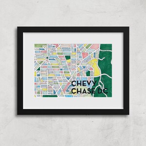 May include: A framed print of a colorful map of Chevy Chase, DC. The map is drawn in a hand-drawn style with different colored blocks representing streets and buildings. The text "CHEVY CHASE DC" is printed in black at the bottom of the map.