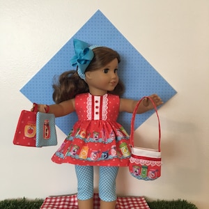 May include: A doll wearing a red dress with a jar pattern, blue polka dot leggings, and blue shoes. The doll has a matching blue bow headband and is holding a red purse and two red bags with jar designs. The doll is standing on a red and white checkered surface.