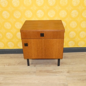 Könnte beinhalten: Ein Vintage-Nachttisch aus Holz in hellem Braun. Er hat eine Schublade und eine Tür, beide mit kleinen, quadratischen schwarzen Griffen. Der Nachttisch steht auf vier schwarzen Beinen und zeigt ein modernes Design aus der Mitte des Jahrhunderts. Maße: 50 cm breit, 40 cm tief, 60 cm hoch.