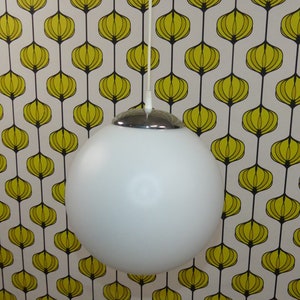 May include: A white globe pendant light with a chrome top, hanging from a white cord against a yellow and black patterned background.
