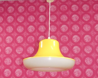 May include: A yellow and white pendant light fixture with a bell-shaped shade hanging from a white ceiling against a pink background with white polka dots.