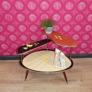 Può includere: Un tavolino da salotto a tre livelli in stile moderno di metà secolo con un piano in nero, rosso e crema. Il tavolino ha un design geometrico con accenti dorati ed è decorato con due gatti in ceramica e due cigni dorati.