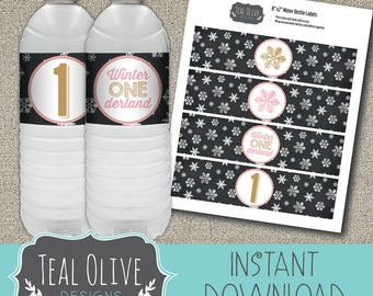 May include: Two water bottles with labels that read "Winter ONE derland" and the number "1". A sheet of matching labels with snowflake patterns and the text "8"x2" Water Bottle Labels" is also visible. The design is by Teal Olive Designs.
