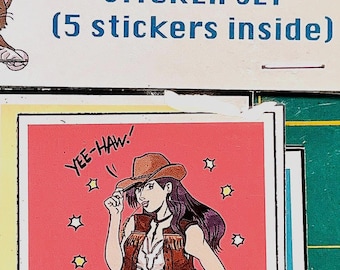 May include: A sticker set labeled "AVALANCHE AMIGOS" with a cartoon cat wearing a crown. The set includes five stickers. One sticker features a cowgirl with the text "YEE-HAW!". The stickers are in a clear plastic sleeve.