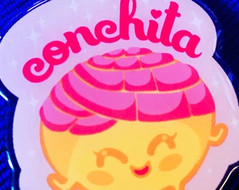 May include: A pink and yellow cartoon conchita keychain with a gold star charm. The keychain features a smiling conchita with pink and white swirls on top. The text "conchita" is written in pink cursive letters.