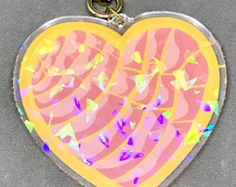 May include: A pink and yellow heart-shaped keychain with a gold star charm. The heart is filled with iridescent glitter and has a swirl pattern.