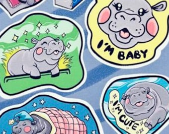 May include: A sheet of stickers featuring cartoon hippos in various poses and settings. The stickers include phrases like "I'm Baby" and "I'm Cute." The artwork is by Andrea Rosales, with a website address at the bottom.