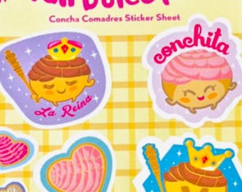 May include: A sticker sheet featuring colorful illustrations of concha pastries with faces and crowns. The sheet includes the text "Pan Dulce Pals" and "Concha Comadres Sticker Sheet". The stickers are on a yellow plaid background.