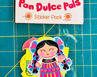 May include: A sticker pack with the title "Pan Dulce Pals" and a sticker of a colorful doll holding a pastry. The doll has black hair, a pink dress, and a blue and yellow skirt. The sticker pack includes other stickers with a yellow background.