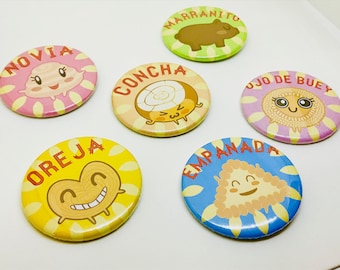 May include: Six colorful round buttons with cartoon images and Spanish text. The buttons feature a pig, a seashell, a pastry, a heart-shaped pastry, a pastry with a swirl design, and a pastry with a triangle shape. The text on the buttons reads "Marranito", "Concha", "Oreja", "Empanada", "Novia", and "Ojo de Buey".