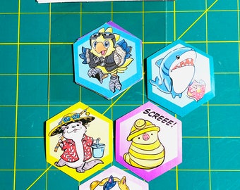 May include: A set of five hexagonal stickers featuring cartoon animal characters. The stickers are printed on white paper with a glossy finish. The characters include a yellow bird wearing goggles, a blue shark, a white and brown otter wearing a red shirt and a straw hat, a yellow and pink striped worm wearing a yellow hard hat, and a white and orange cat lying on a pink cloud. The stickers are labeled "Fantasy Friends Sticker Set (5 stickers inside)".