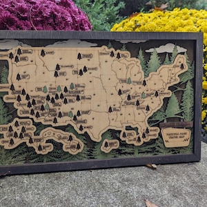 May include: A wooden map of the United States with a brown frame. The map shows the locations of National Parks across the country. The text "National Parks Travel Map" is printed in the lower right corner of the map.
