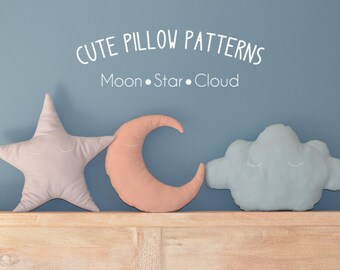 May include: Three plush pillows shaped like a star, crescent moon, and cloud. The pillows are light pink, peach, and light blue. The pillows have embroidered eyes and are arranged on a wooden shelf against a blue wall. The text "CUTE PILLOW PATTERNS Moon.Star.Cloud" is above the pillows.