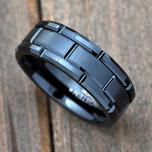 May include: A black tungsten carbide ring with a grooved design. The ring has a brushed finish and a beveled edge.