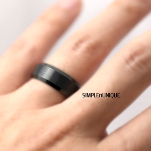 May include: A black tungsten carbide ring with a brushed finish. The ring is worn on a finger.