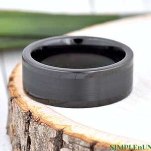 May include: A black tungsten carbide ring with a brushed finish. The ring has a beveled edge and a polished inner surface.