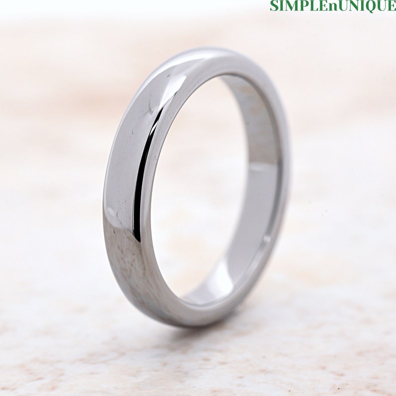 May include: A silver-toned wedding band with a polished finish. The band is simple and elegant, with a smooth, rounded surface.