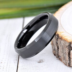 May include: A black tungsten carbide ring with a beveled edge and a brushed finish.