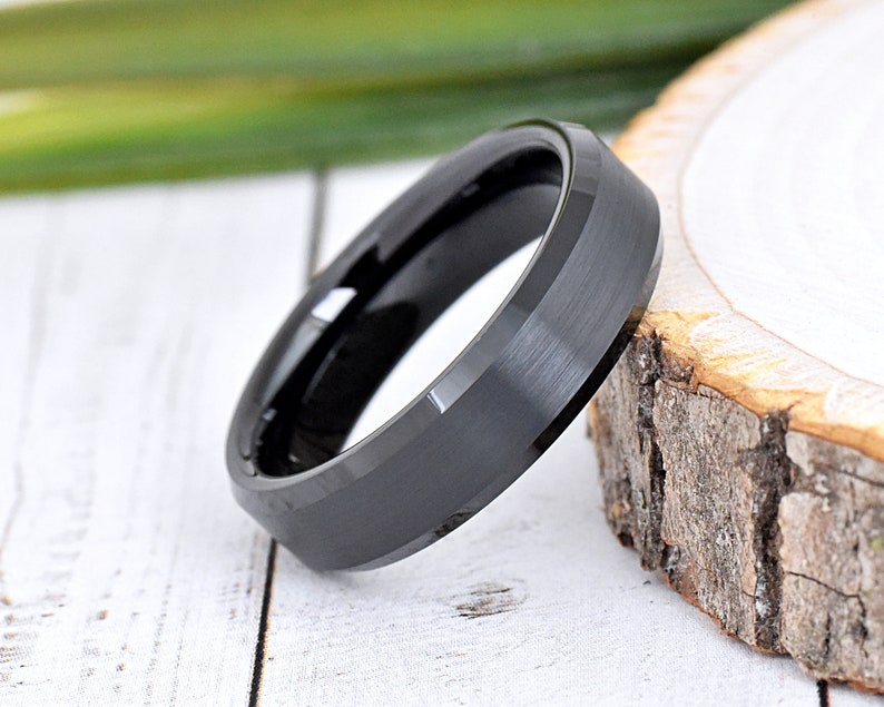 May include: A black tungsten carbide ring with a beveled edge and a brushed finish.