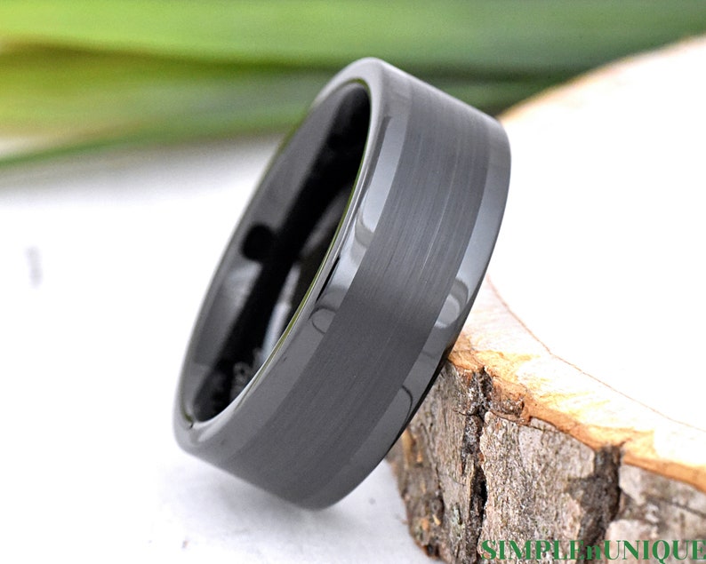 May include: A black tungsten carbide ring with a brushed finish and a beveled edge.
