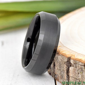 May include: A black tungsten carbide ring with a beveled edge and a brushed finish.