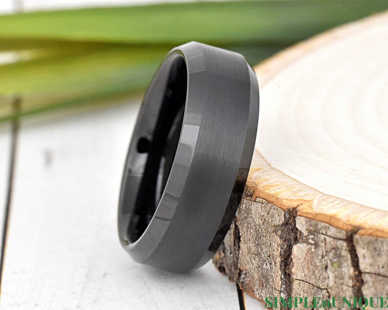 May include: A black tungsten carbide ring with a beveled edge and a brushed finish.