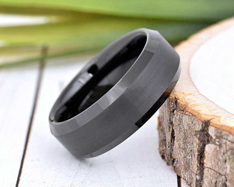 May include: A black tungsten carbide ring with a beveled edge and a brushed finish.