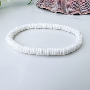 Puede incluir: Un brazalete blanco de conchas hecho de pequeñas conchas redondas. El brazalete es simple y elegante, perfecto para un look playero.