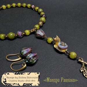 May include: A handmade jewelry set featuring a necklace, earrings, and a pendant. The necklace and pendant have green beads and a snail charm. The earrings have purple and green flower-shaped beads. The set is displayed on a dark surface. The text "Design by Polina Petrovets" is visible.