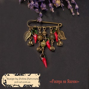 Könnte beinhalten: Eine Brosche im Vintage-Stil mit Sicherheitsnadelverschluss. Die Brosche hat hängende Anhänger, darunter rote Chilischoten, kleine Kürbisse und blattförmige Anhänger. Das Design umfasst grüne und braune Perlen. Der Text "Design by Polina Petrovets" ist sichtbar.