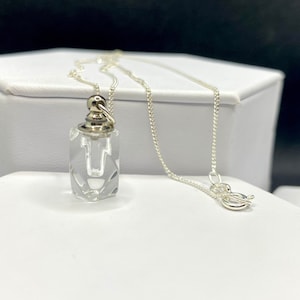May include: A silver chain necklace with a clear glass pendant shaped like a bottle. The pendant has a silver cap and a silver loop for attaching to the chain.