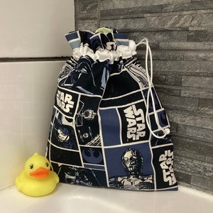 Peut inclure: Un sac à cordon bleu et noir sur le thème de Star Wars. Le sac présente des images de Dark Vador, C-3PO et du Faucon Millenium. Le sac est posé sur une surface blanche.