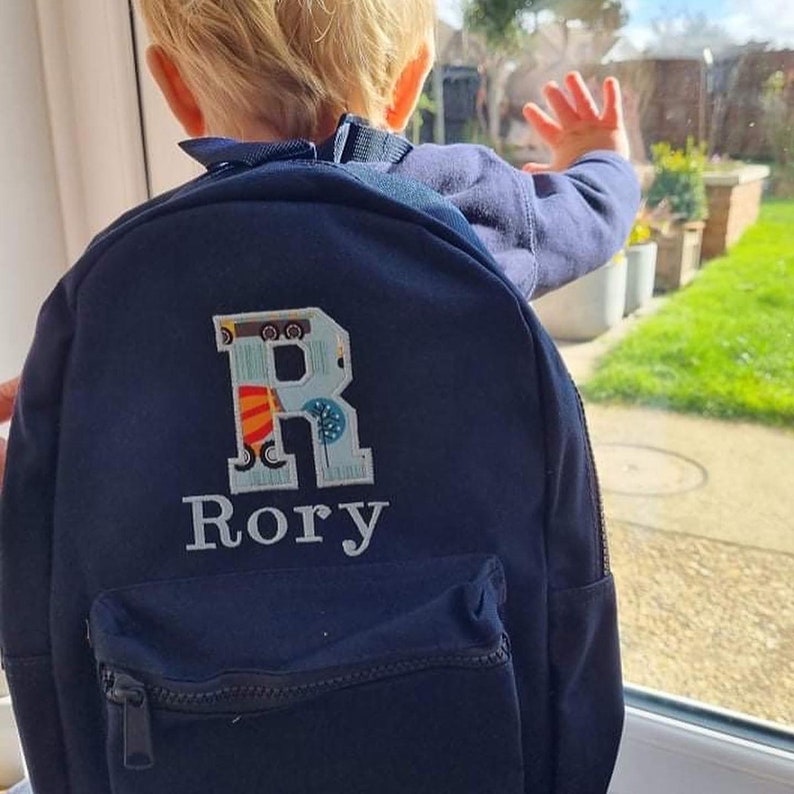 May include: A navy blue backpack with a large, colorful letter "R" and the name "Rory" embroidered on the front.