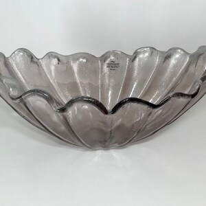 May include: A large, clear glass bowl with a scalloped edge and a rippled design. The bowl is a light purple color and has the word "MIRRORS" printed on the bottom.